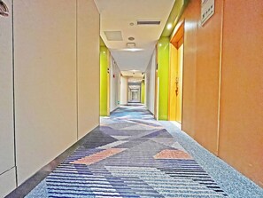 Un pasillo de hotel con alfombra estampada, puertas a la derecha y un letrero a la izquierda.