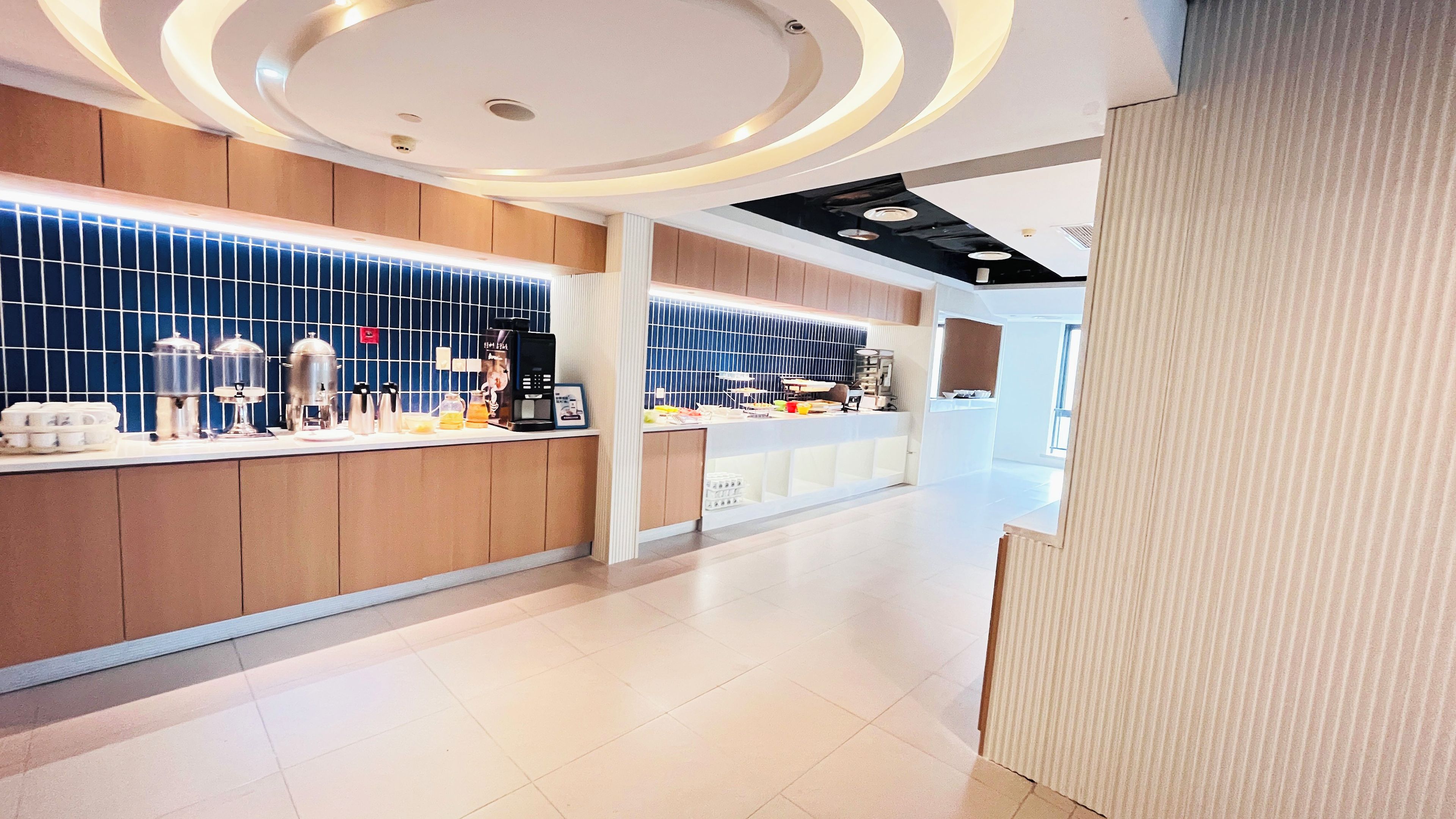 A modern hotel lobby with a reception desk, a coffee machine, and a wall-mounted kettle.