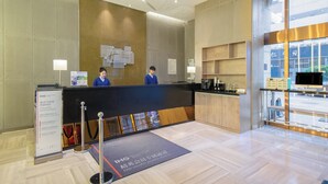 A hotel reception area with a reception desk, two staff members, a coffee machine, and a display of amenities. - Holiday Inn Express Changzhou Center by IHG (Changzhou)