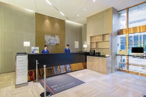 A hotel reception area with a reception desk, two staff members, a coffee machine, and a display of amenities. - Holiday Inn Express Changzhou Center by IHG (Changzhou)