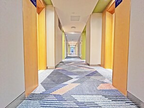 Pasillo de hotel con alfombra estampada, puertas a ambos lados y un cartel con los números de las habitaciones.