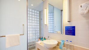Un baño moderno con un espejo grande, un lavamanos blanco y una cabina de ducha de vidrio.