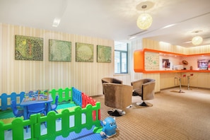 A children's play area with a blue table, colorful building blocks, and a blue toy. There are two brown chairs and a large orange counter with a map. - Holiday Inn Express Changzhou Center by IHG (Changzhou)