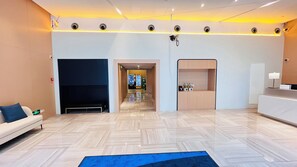 Un hall d’hôtel comprenant un comptoir d’accueil, un espace salon et un couloir menant à une chambre.