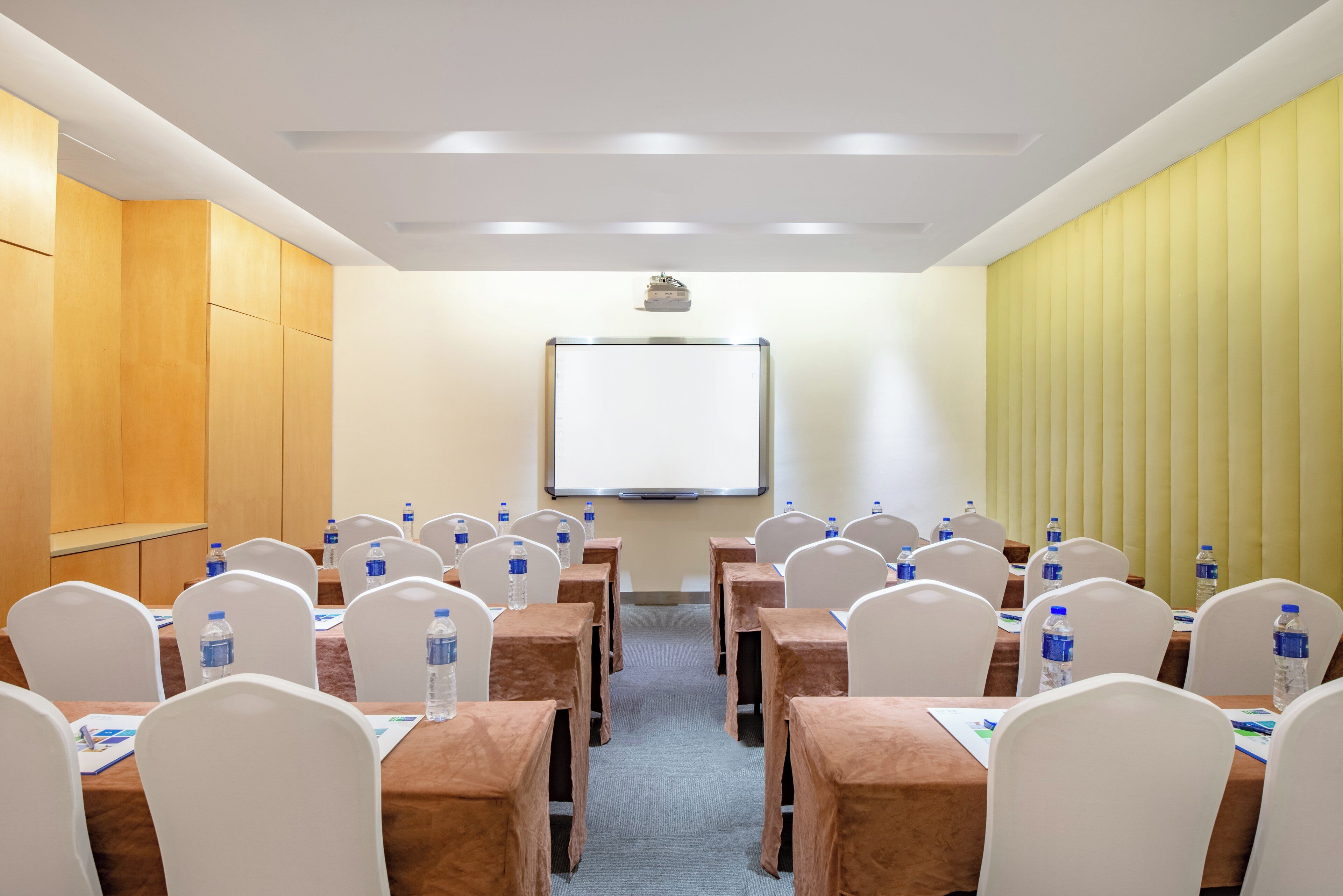 Un salón de conferencias con mesas, sillas y una pantalla para proyector.