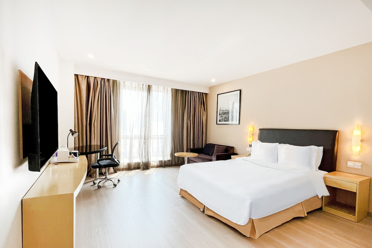 A hotel room with a bed, a desk, a chair, a television, and a window with curtains.