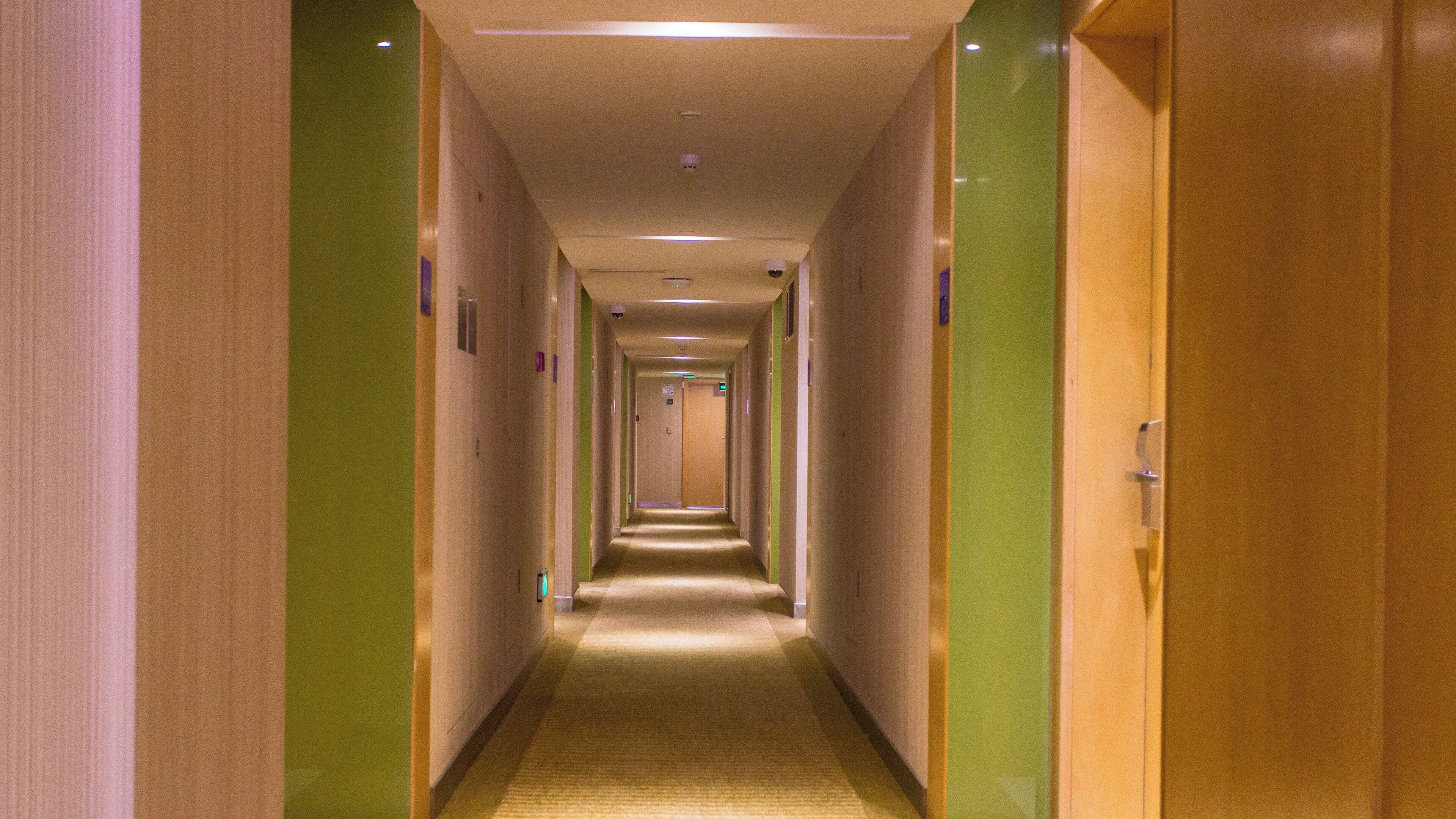 Un couloir d’hôtel avec des portes des deux côtés, un sol recouvert de moquette et un éclairage au plafond.