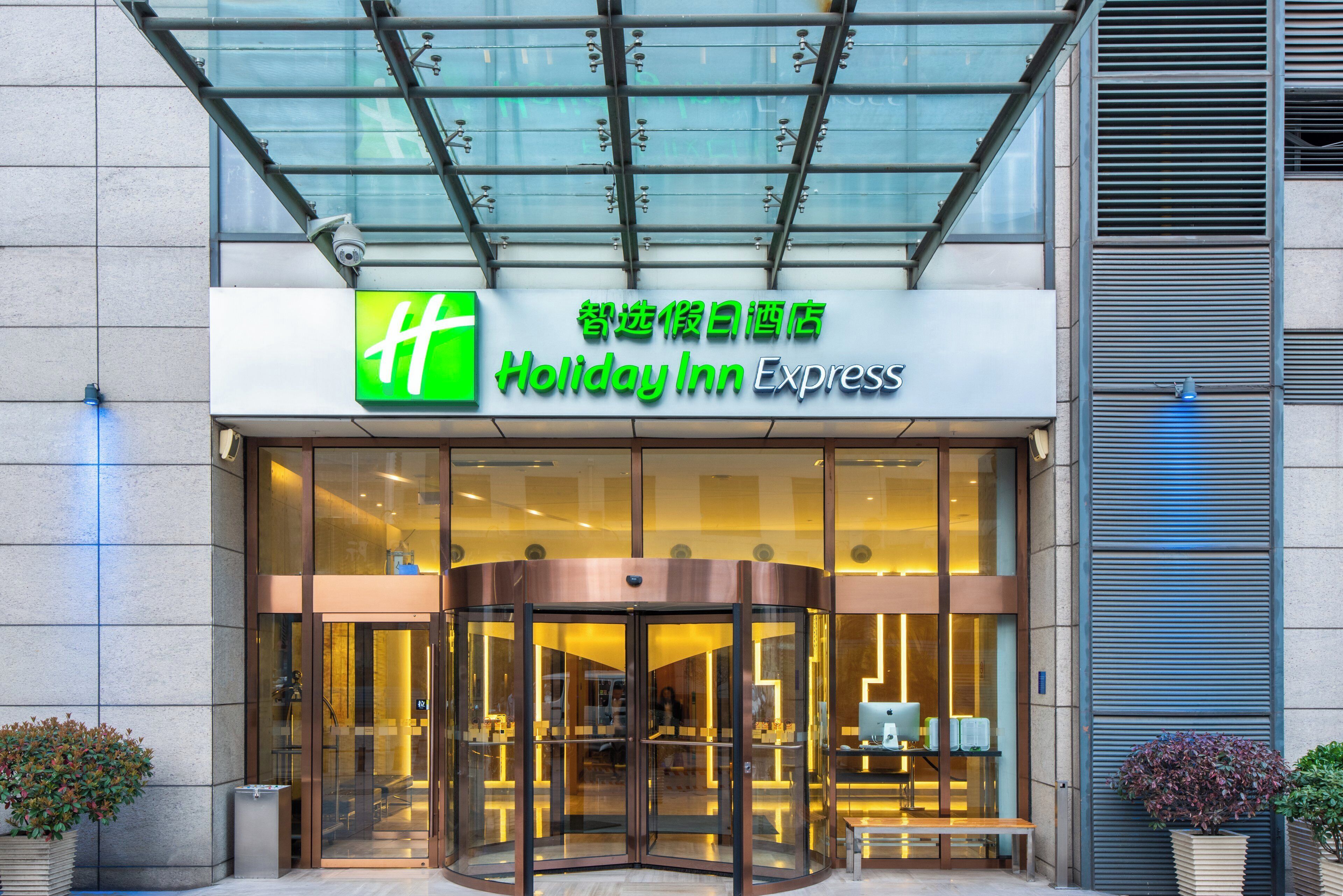 L’entrée d’un hôtel Holiday Inn Express, avec une façade en verre, une porte tournante et une enseigne en anglais et en chinois.