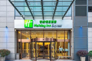 L’entrée d’un hôtel Holiday Inn Express, avec une façade en verre, une porte tournante et une enseigne en anglais et en chinois.