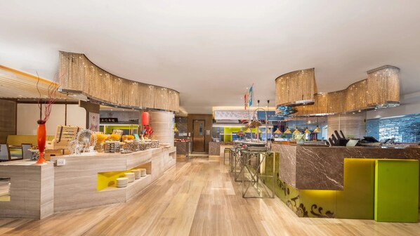 Ein modernes Restaurant mit einem zentralen Essbereich, einer Bar und einer im Hintergrund sichtbaren Küche.