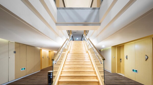 Un couloir d’hôtel moderne avec un escalier central en bois, des rampes de protection en verre et un revêtement de sol en bois.