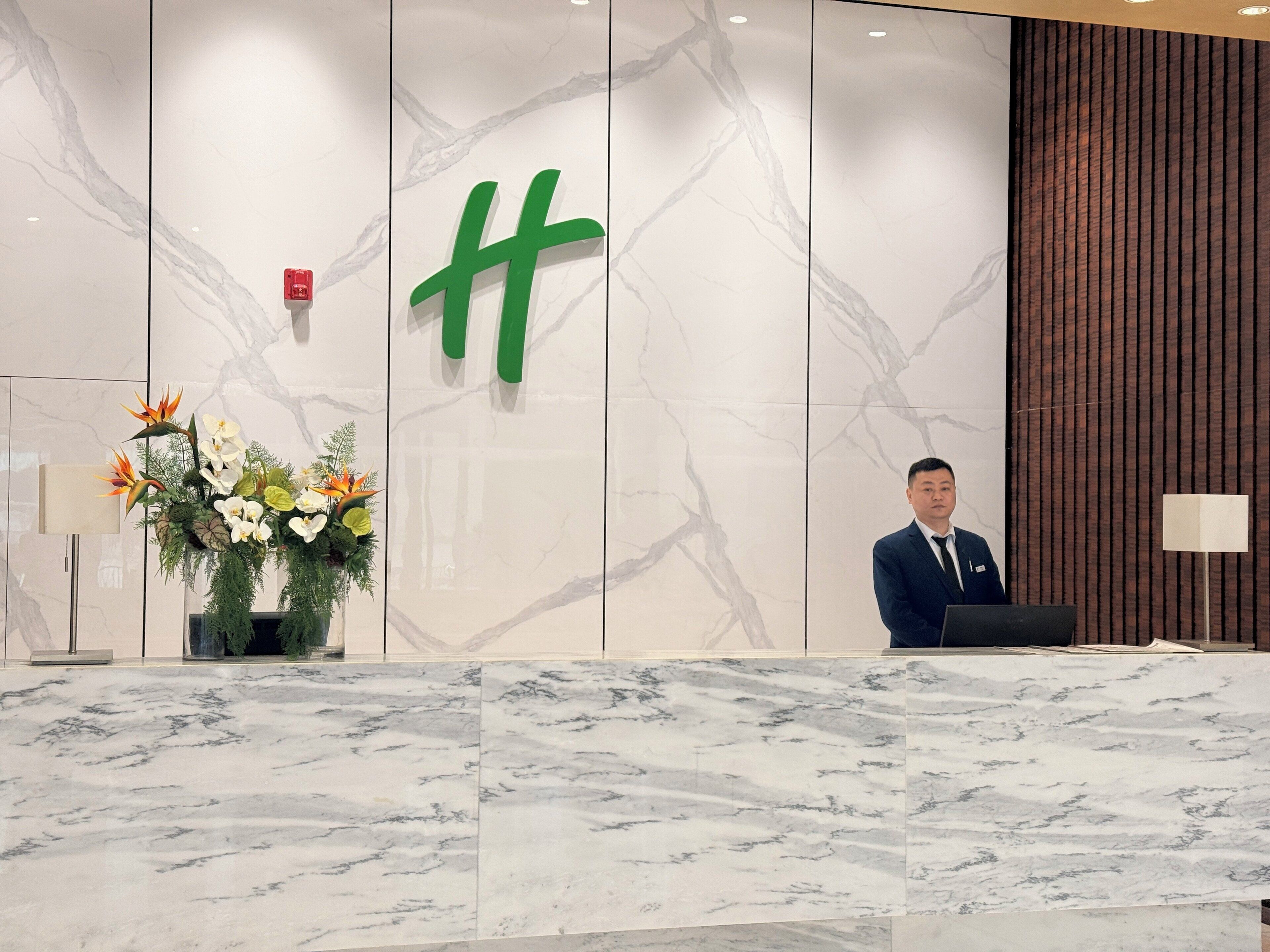 Una recepción con encimera de mármol, una gran letra 'H' verde en la pared y un arreglo floral.
