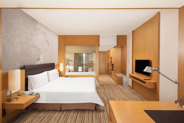 A hotel room with a large bed, bedside tables, a TV, and a bathroom visible through a glass door.