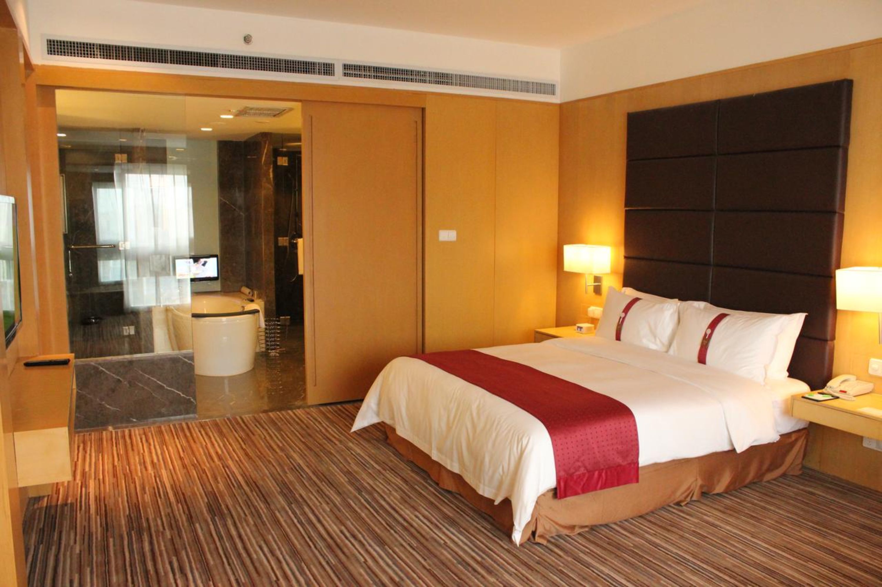 A hotel room with a large bed, a bedside table with a lamp, a mirror, and a view of a bathroom.