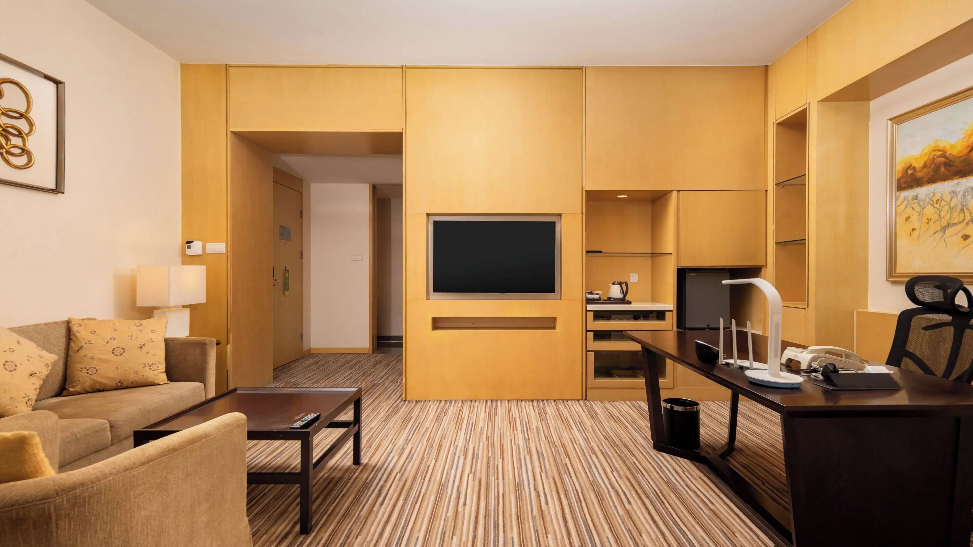 Een hotelkamer met een bank, een bijzettafeltje, een televisie, een bureau met een computer en een schilderij aan de muur.