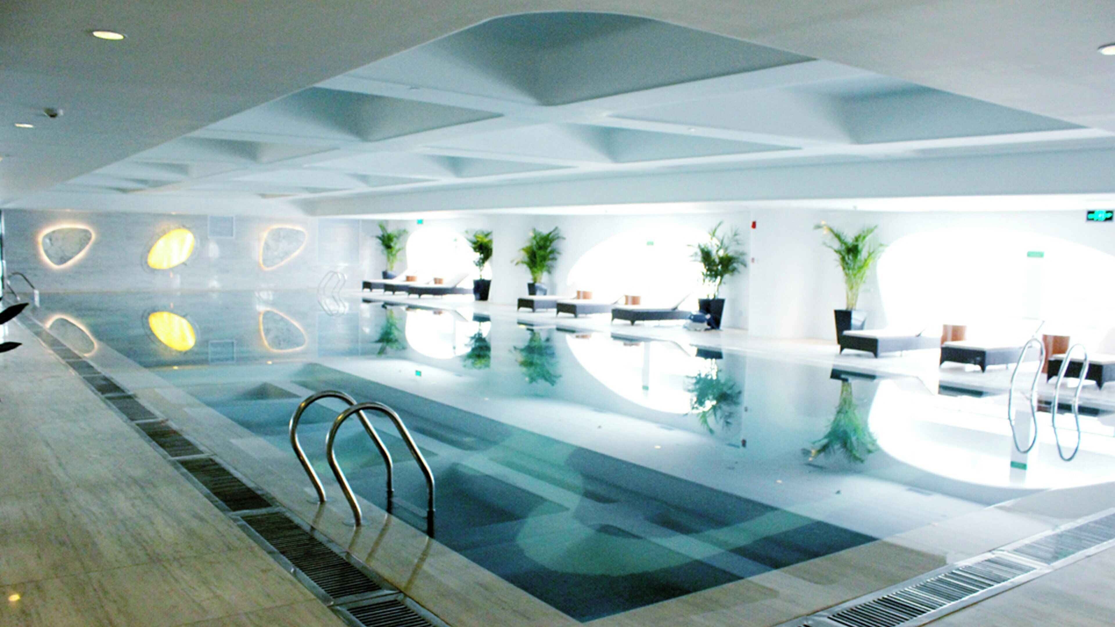 Ein moderner, überdachter Pool mit klarem Wasser, Liegestühlen und Zimmerpflanzen.