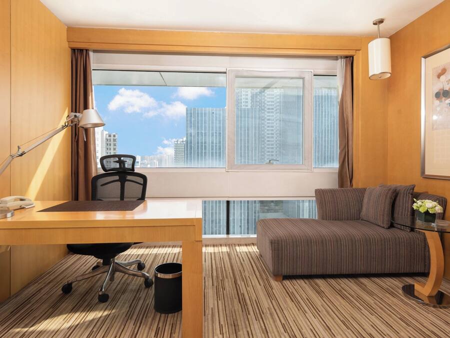 Ein Hotelzimmer mit Schreibtisch, Stuhl, Sofa und einem großen Fenster mit Blick auf die Stadt.