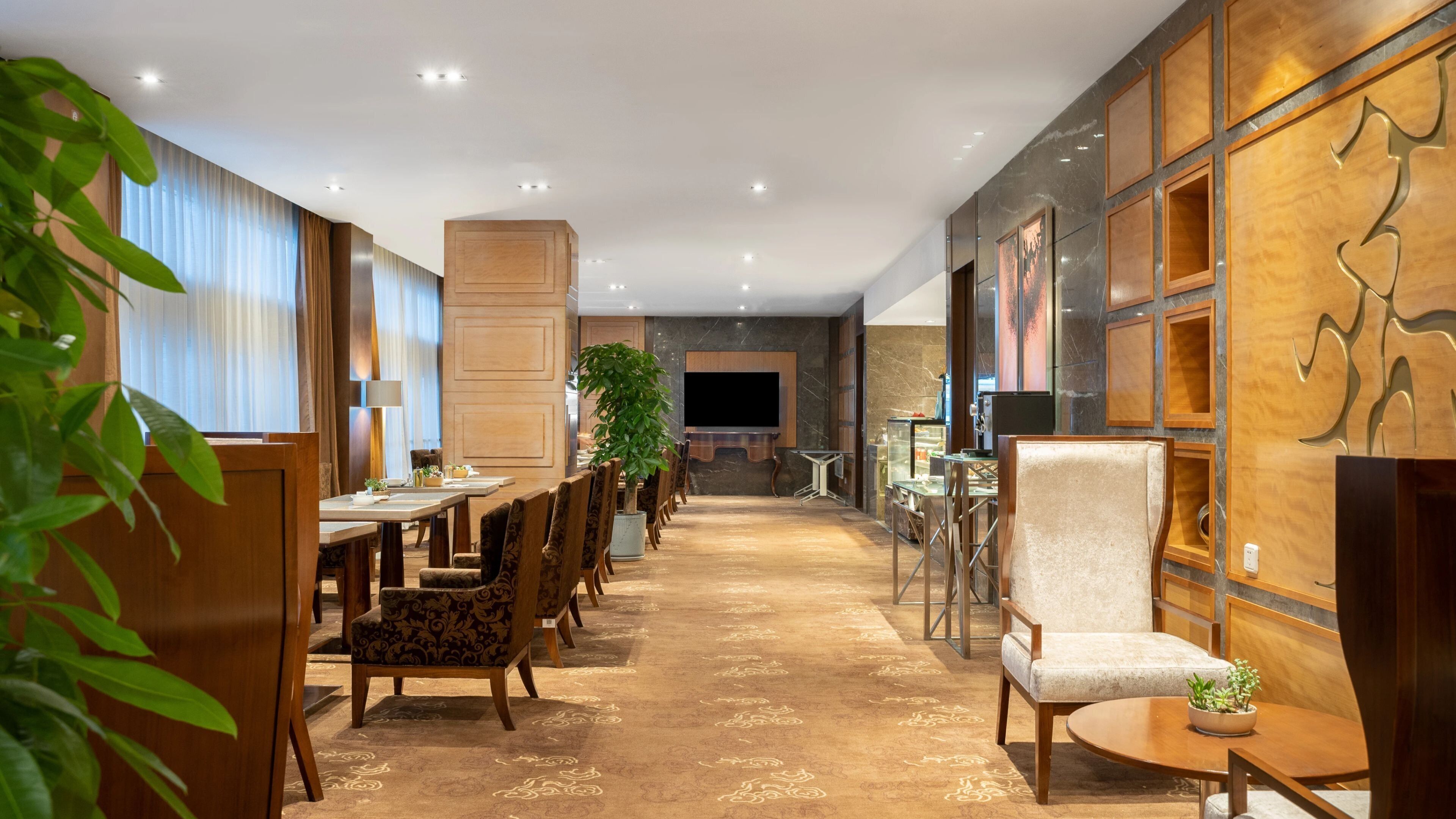 Un vestíbulo de hotel con una larga mesa de comedor, numerosas sillas, un televisor grande y paneles decorativos en la pared.