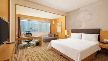 A hotel room with a large bed, a desk with a chair, a TV, and a window with curtains.