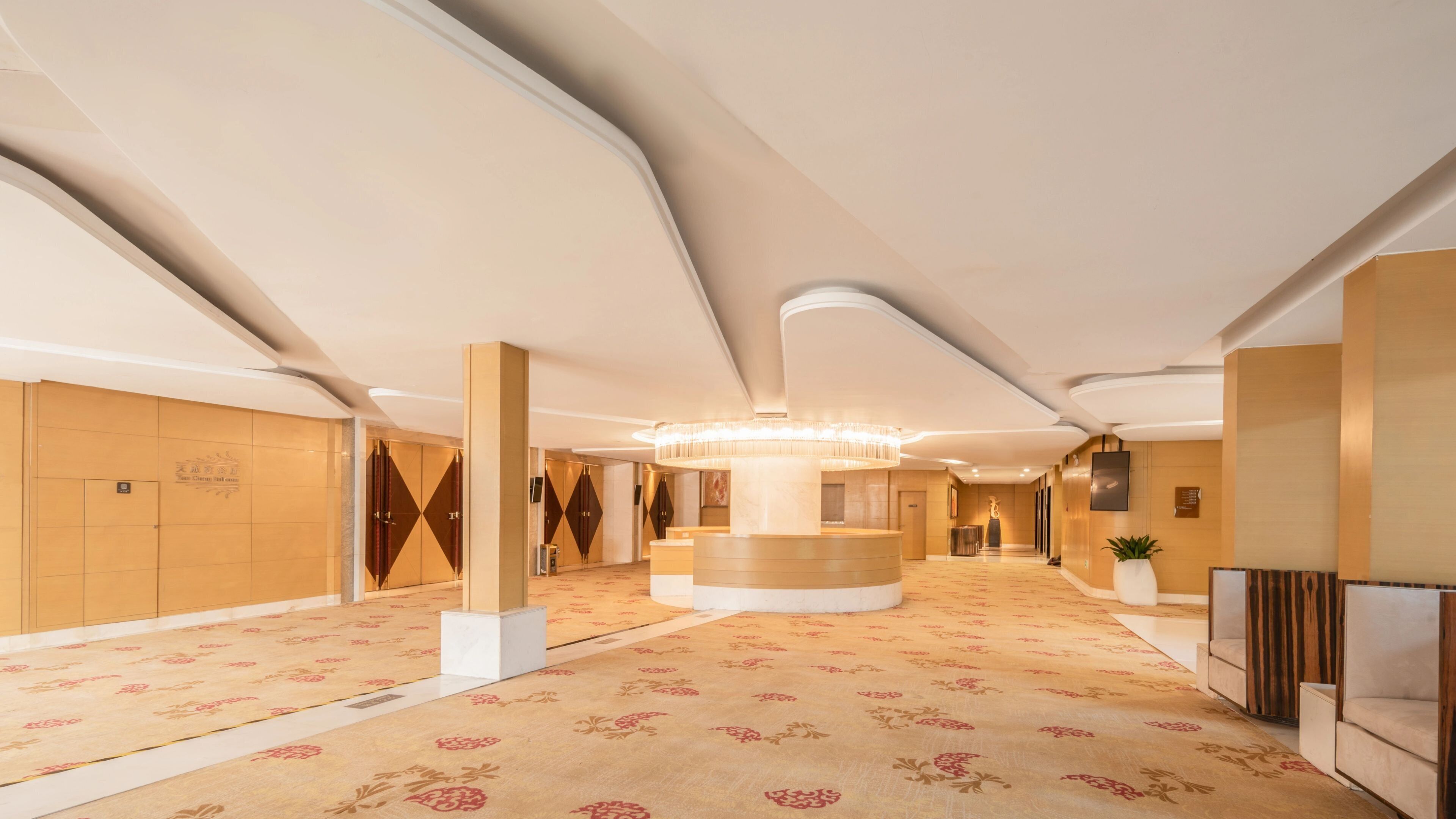 Un hall d’hôtel spacieux, doté d’un comptoir d’accueil central, de hauts plafonds et d’un tapis à motifs.