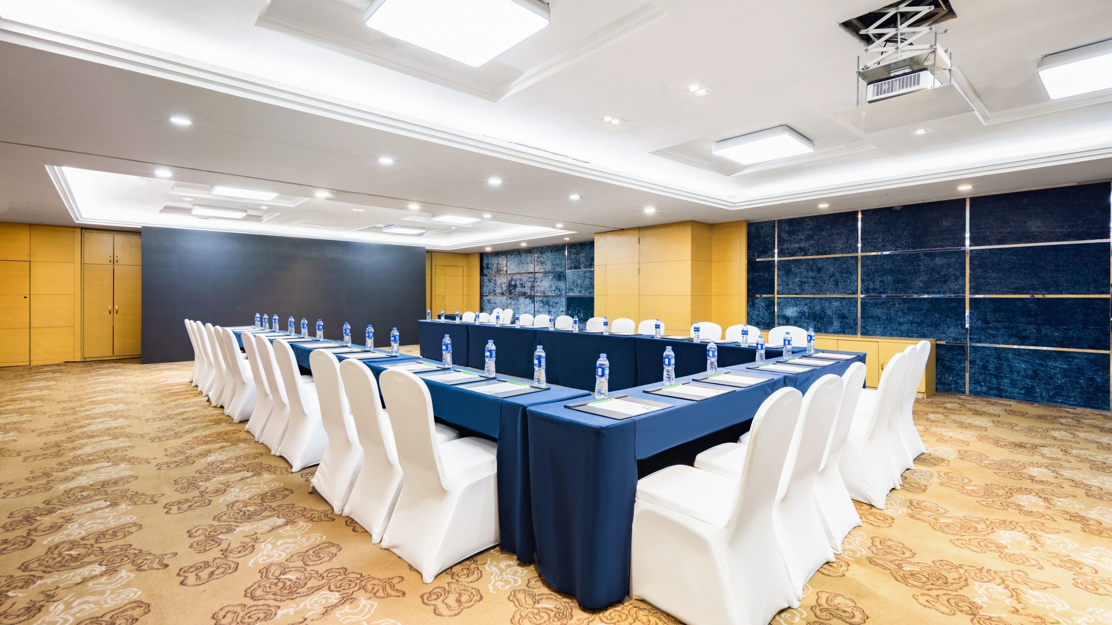 Un salón de conferencias con una larga mesa, sillas blancas y botellas de agua.