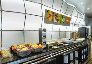 Un espace buffet proposant une variété de plats, notamment du pain, des pâtisseries et un coin café.