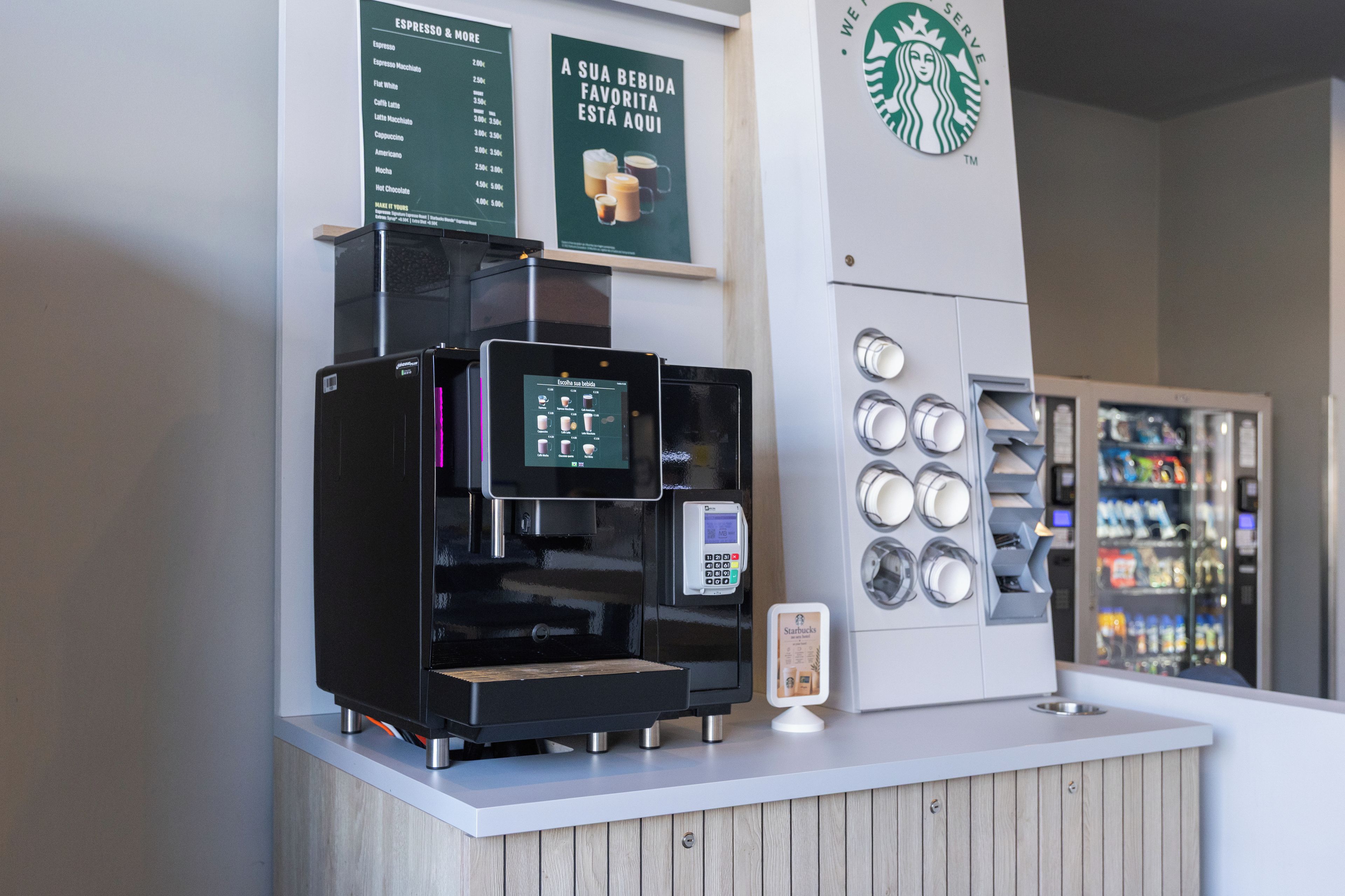 Una máquina de café con pantalla digital, un menú en la parte superior y el logotipo de Starbucks en la pared.