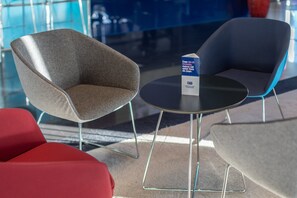 A modern seating area with two chairs and a table, a sign with text, and a glass partition in the background. - Holiday Inn Express Lisbon - Alfragide by IHG (Oeiras)