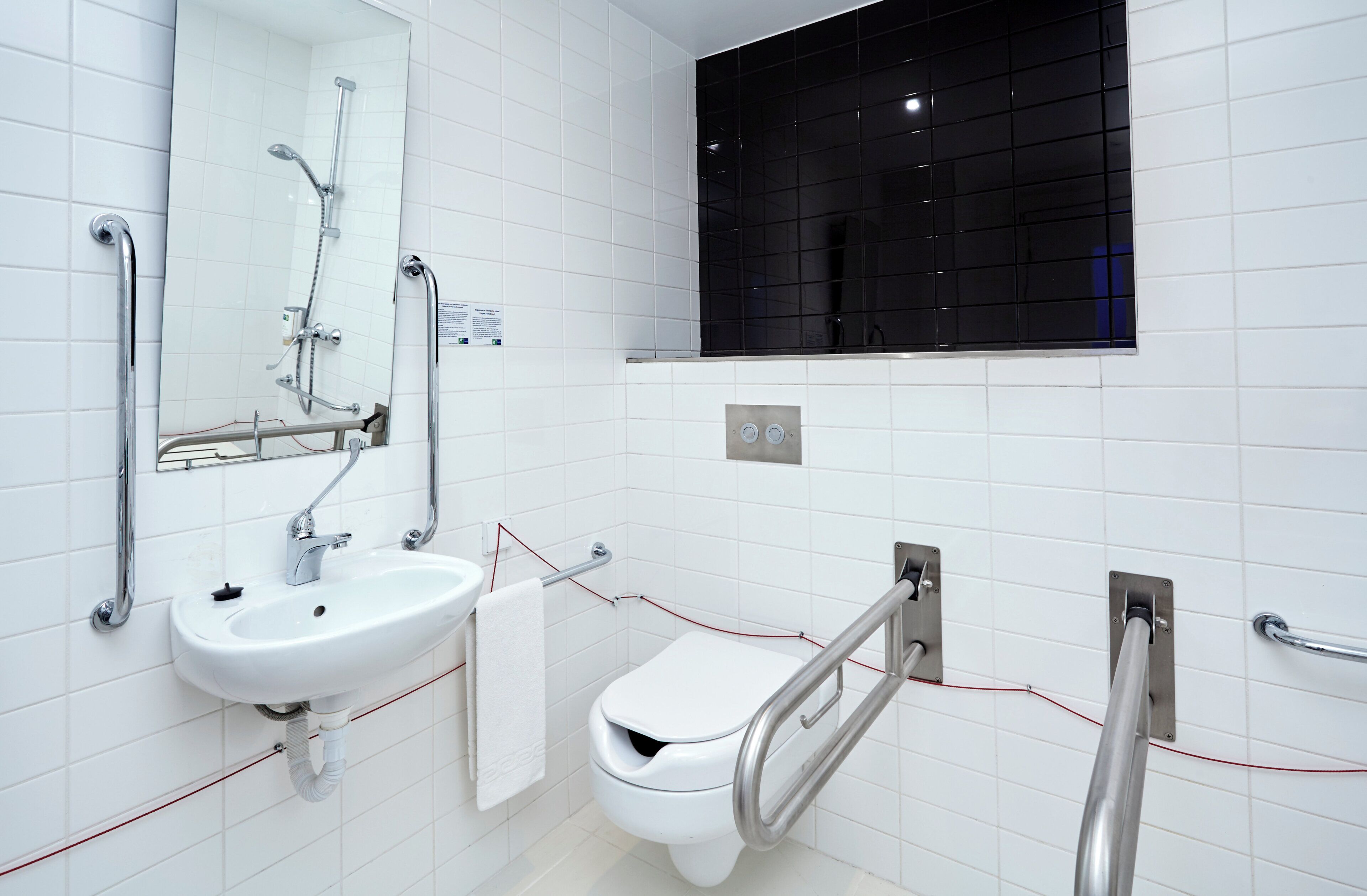 A modern bathroom with a white sink, a mirror, a toilet, and a shower area.