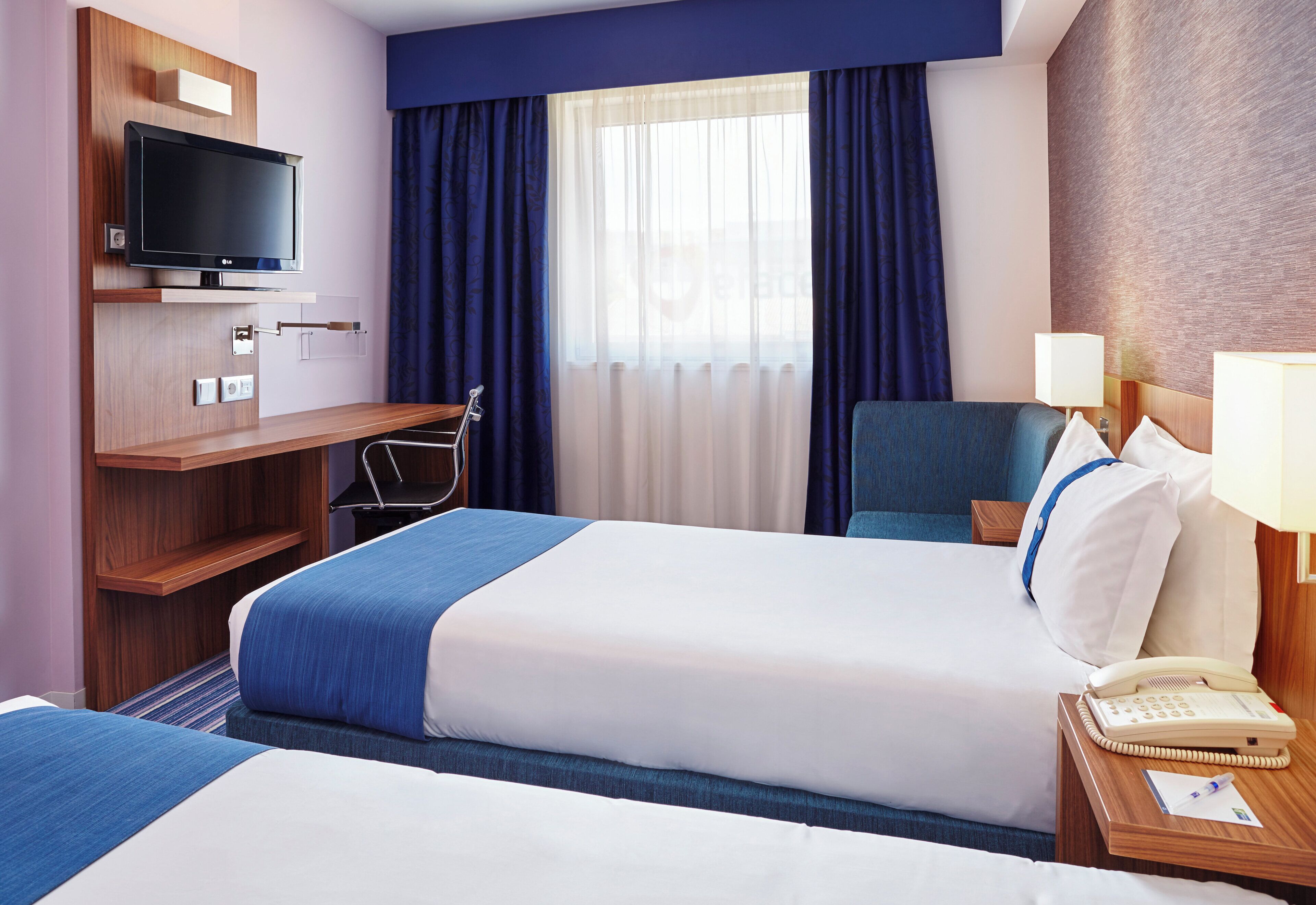 A hotel room with a bed, a desk, a chair, a television, and a telephone.