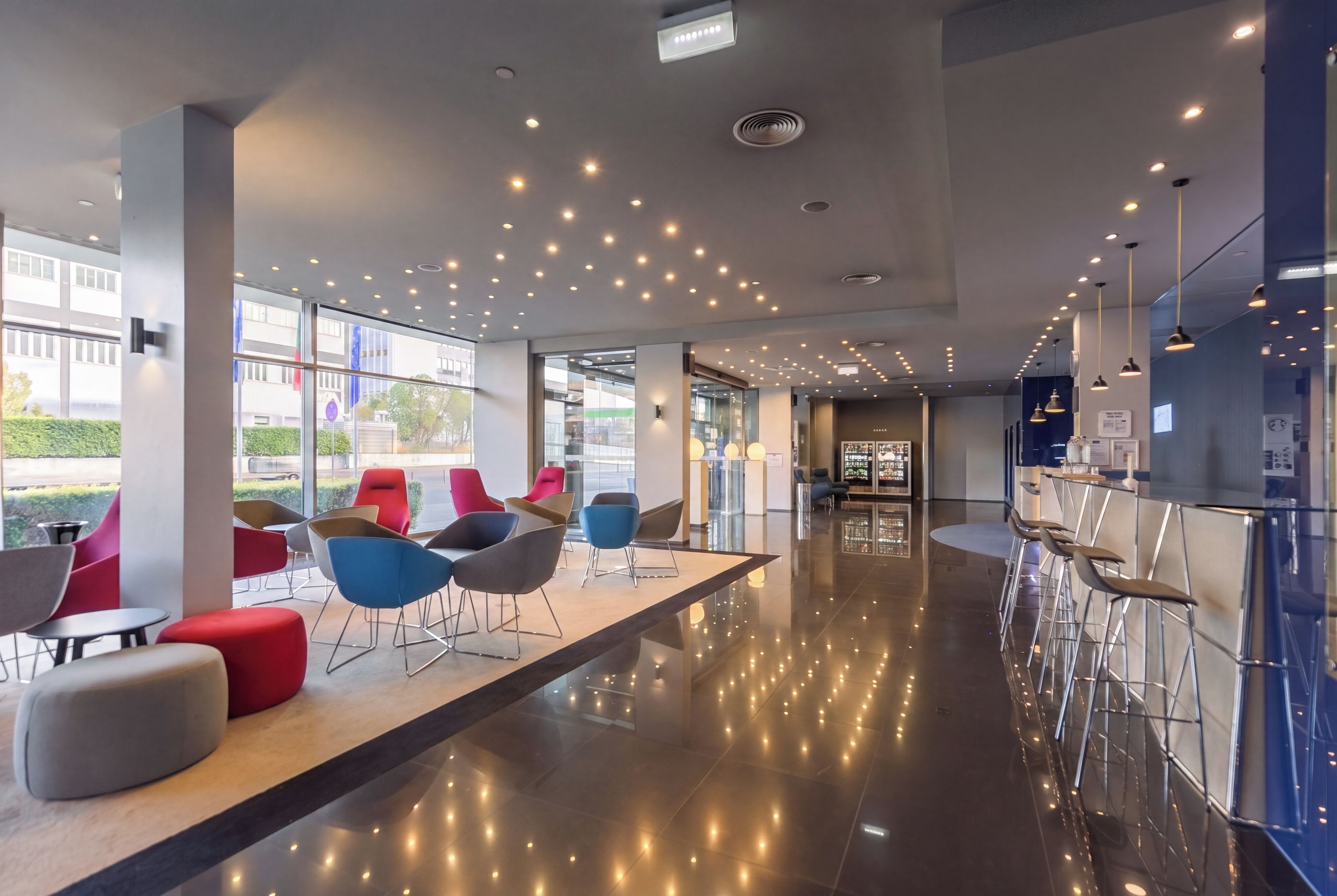 A modern interior with a long reception area, seating with metal frames, and a glass partition.