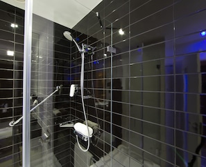 A modern bathroom with black tiled walls, a glass shower enclosure, and a handheld showerhead. - Holiday Inn Express Lisbon - Alfragide by IHG (Oeiras)