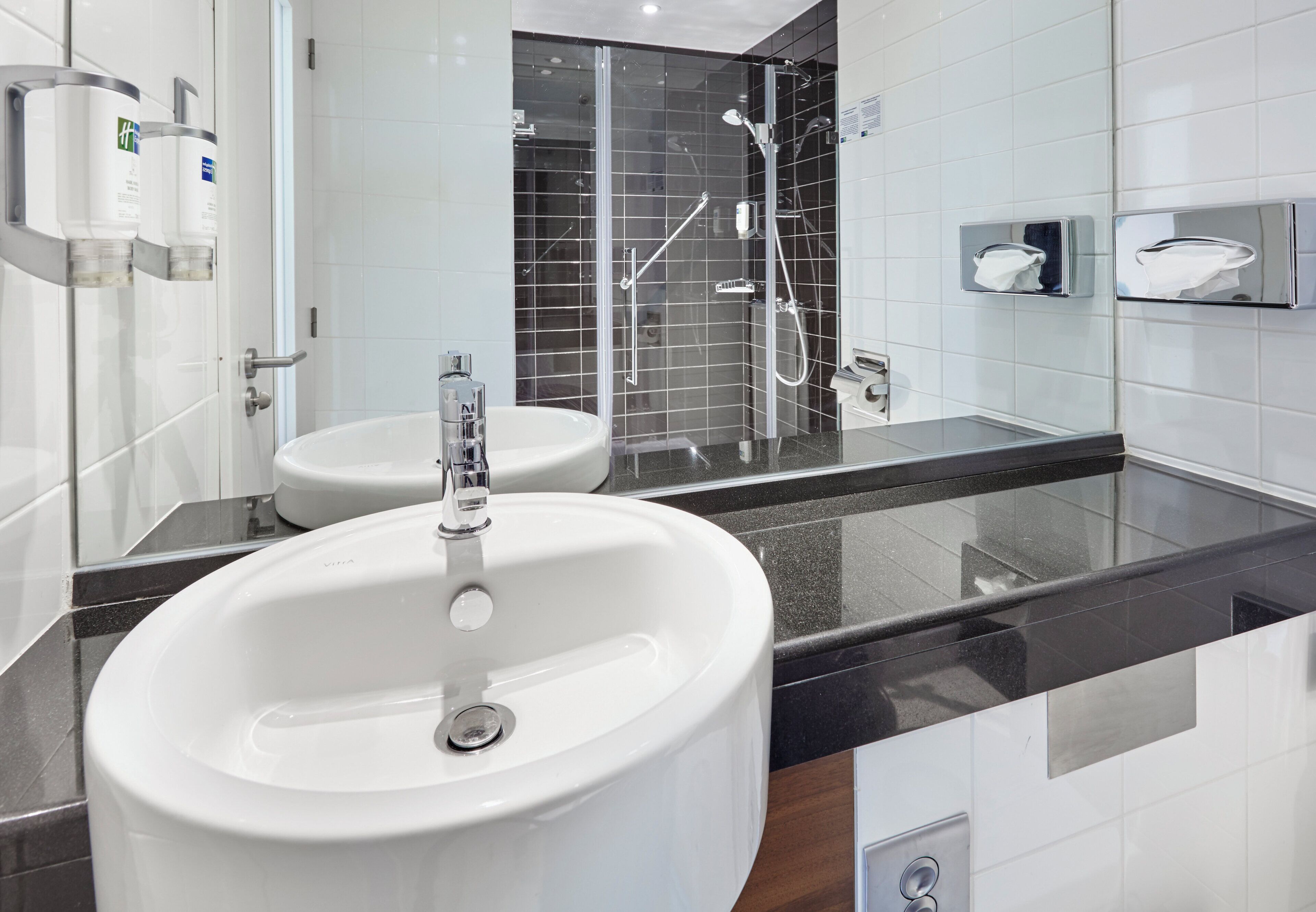 Ein modernes Badezimmer mit einem großen, weißen Waschbecken, einem kleineren Waschbecken und einer Duschkabine aus Glas.