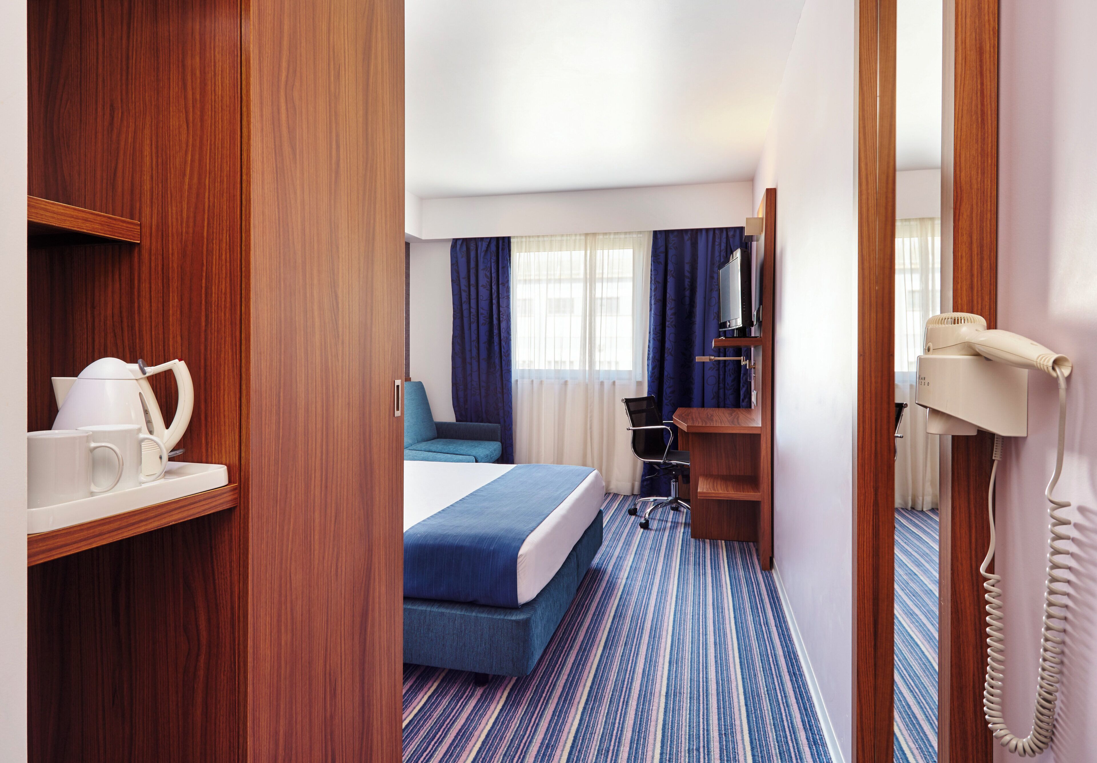 Quarto de hotel com cama, escrivaninha, cadeira, telefone e cafeteira.
