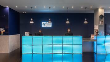 A Holiday Inn Express reception desk with a blue-tiled counter, overhead lighting, and a clock on the wall.
