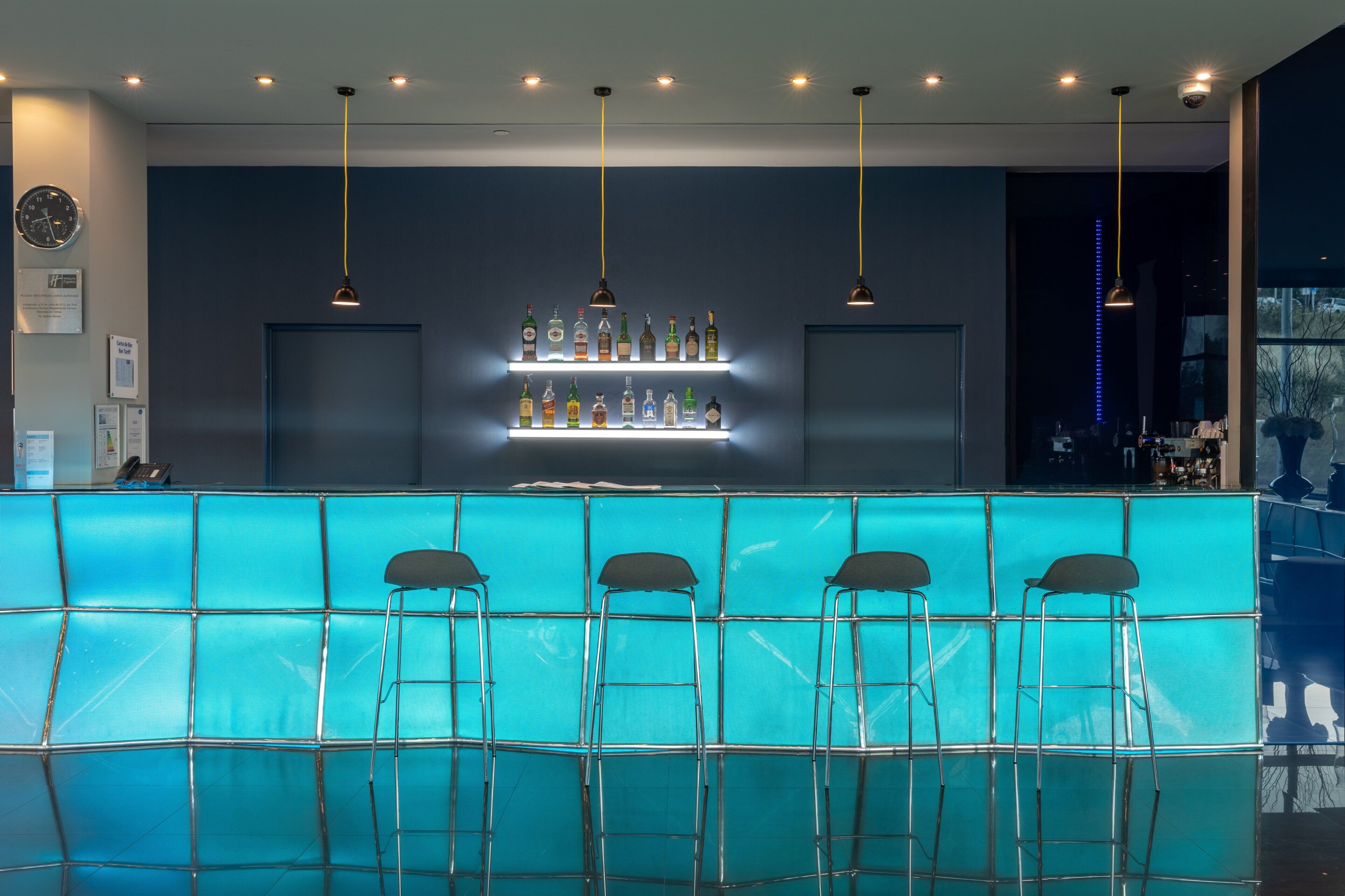 Zona de bar con mostrador azul, varias luces colgantes y taburetes.