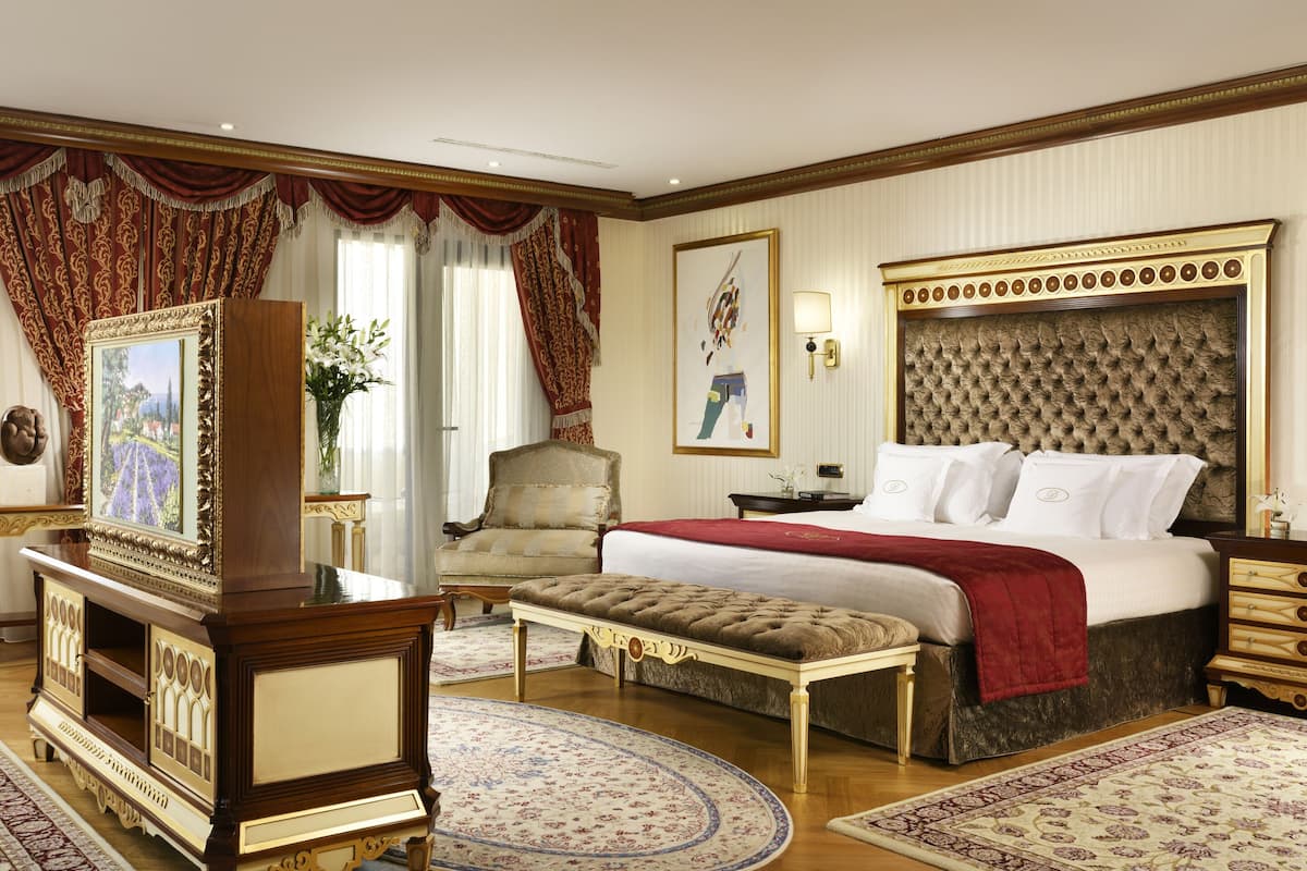 A spacious hotel room with a large bed, a sitting area with a bench, a television, and a decorative fireplace.