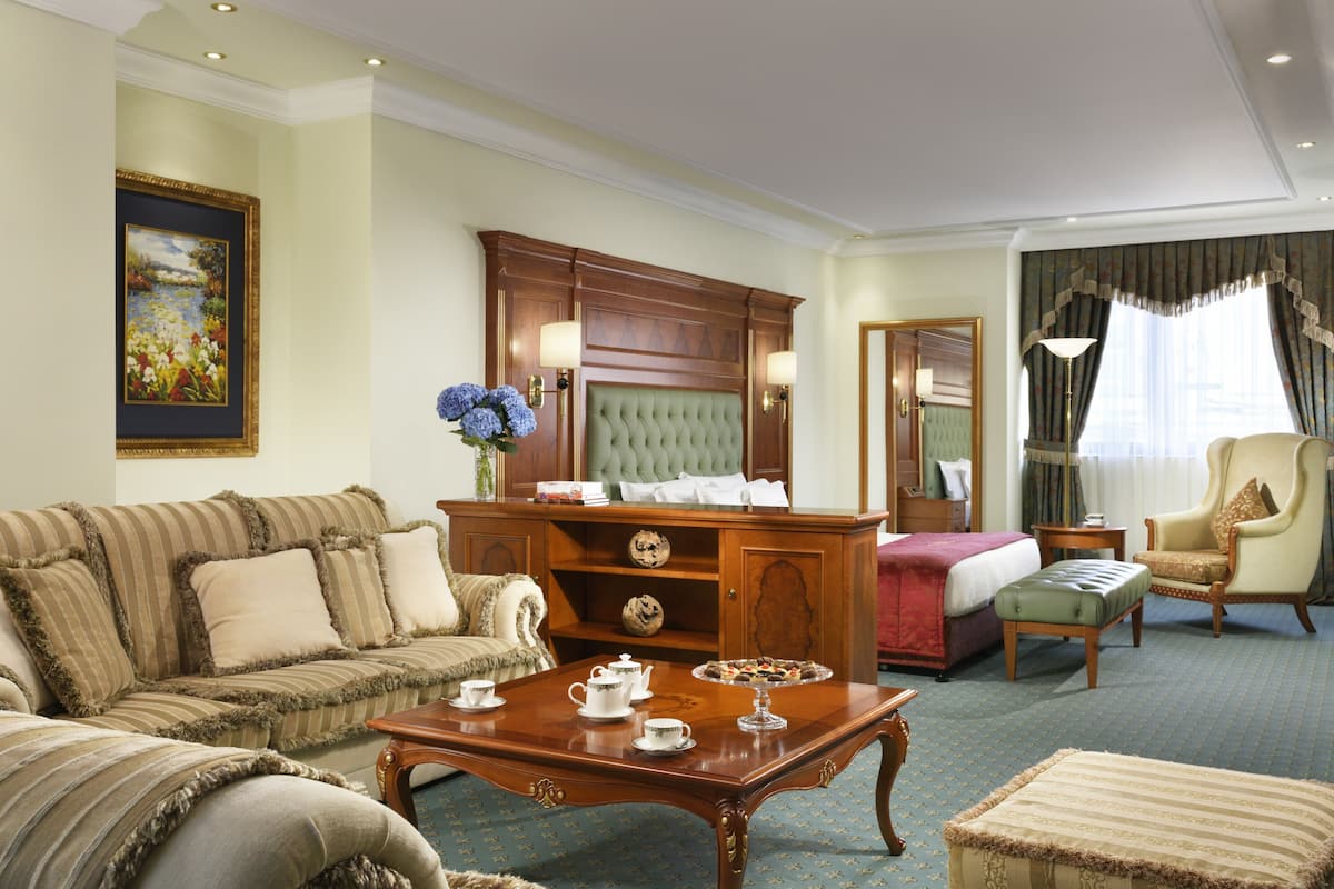 A hotel room with a large bed, a sofa, a wooden coffee table, and a chair.