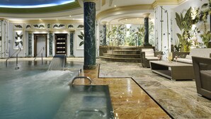 A luxurious indoor pool area with a marble floor, seating by the pool, and a large decorative column. - Swiss Diamond Hotel Prishtina (Pristina)