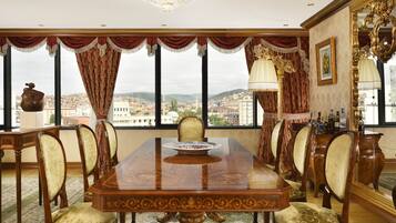 Ein Esszimmer mit einem großen Holztisch, verzierten Stühlen und Blick auf eine Stadtlandschaft durch große Fenster.