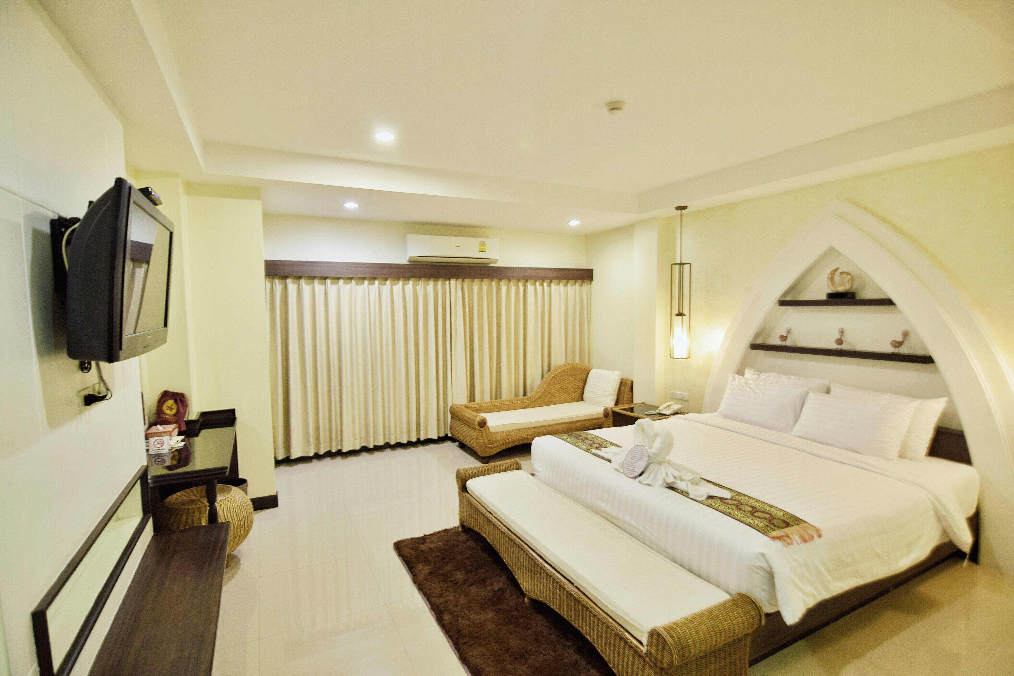 A hotel room with a large bed, a sofa, a television, and a window with curtains.