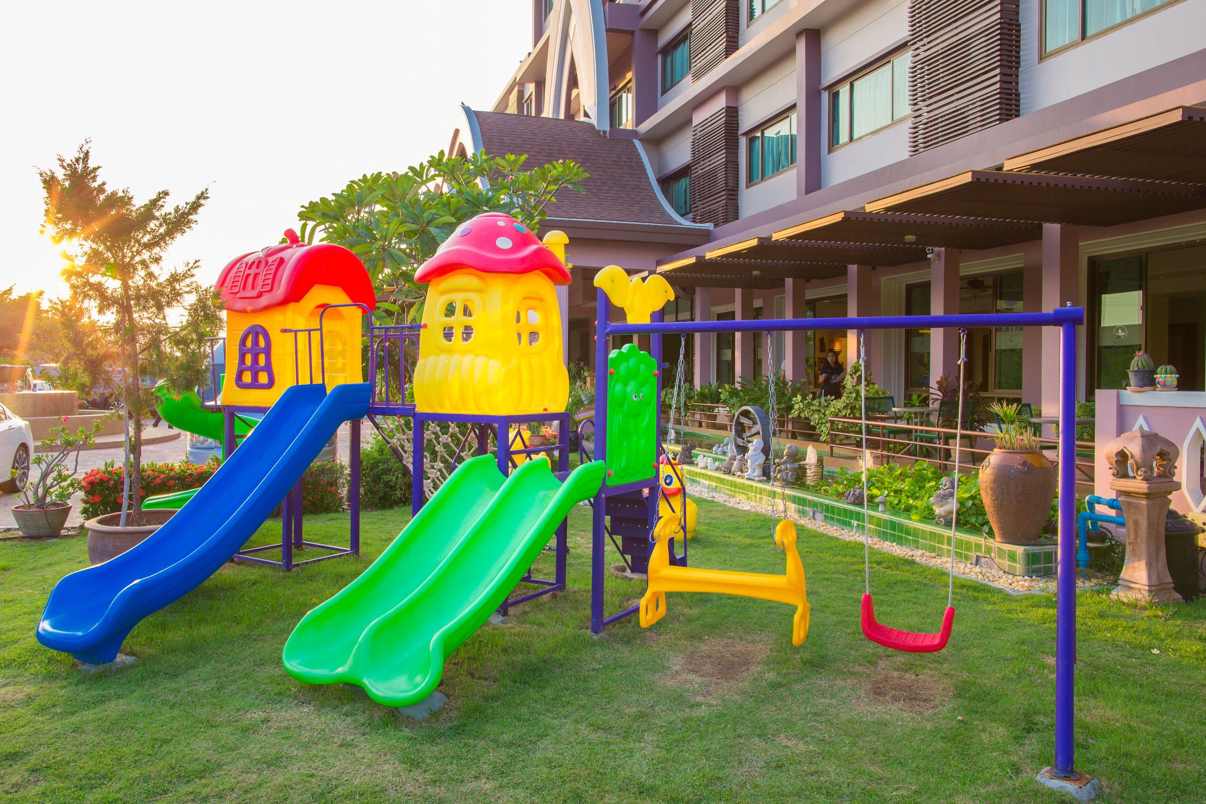 A playground with slides and swings, surrounded by a building with balconies and windows.