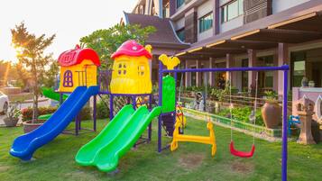 A playground with slides and swings, surrounded by a building with balconies and windows.
