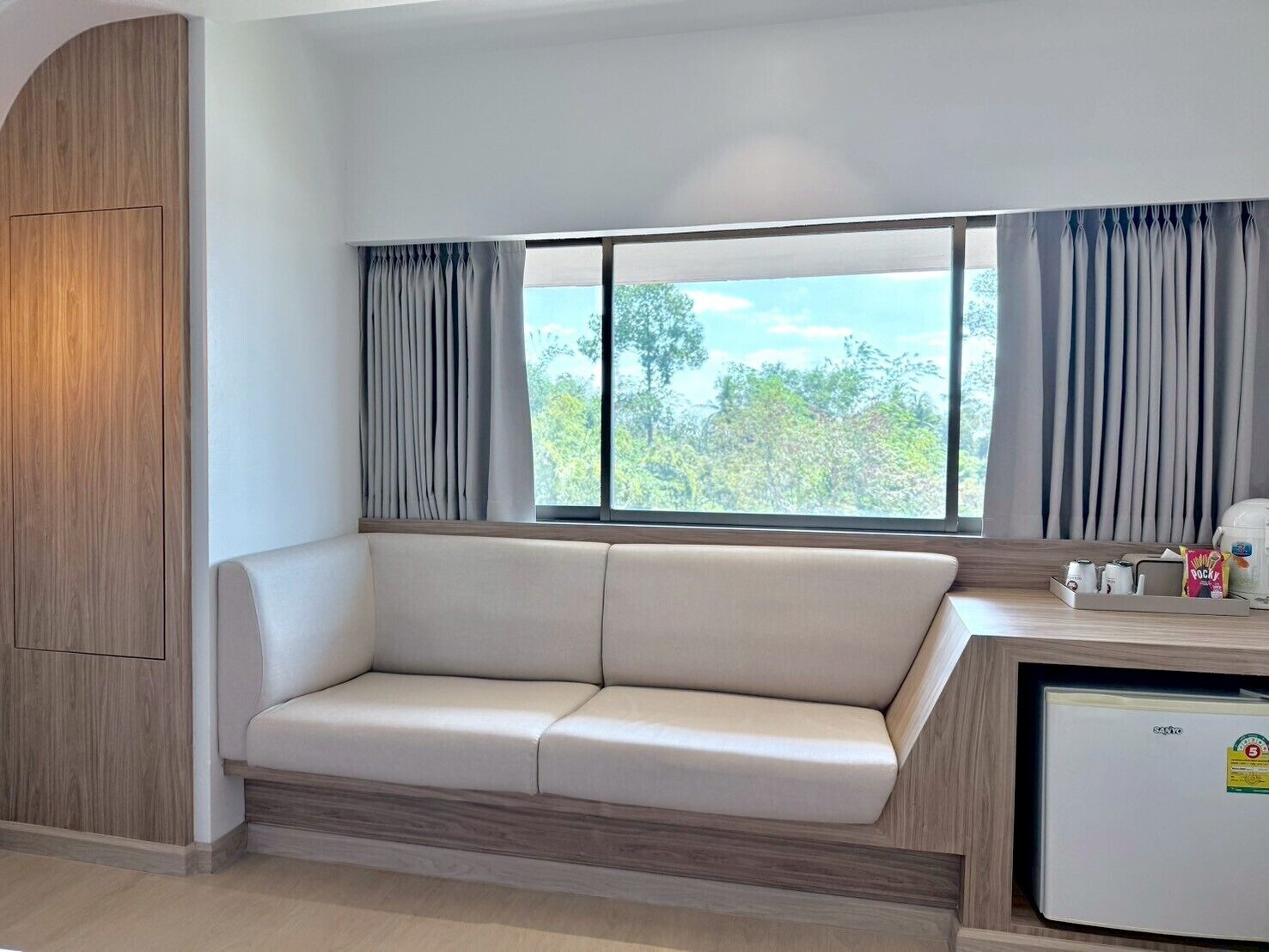 Una kitchenette moderna con un refrigerador empotrado, una pequeña encimera y un ventanal con cortinas.