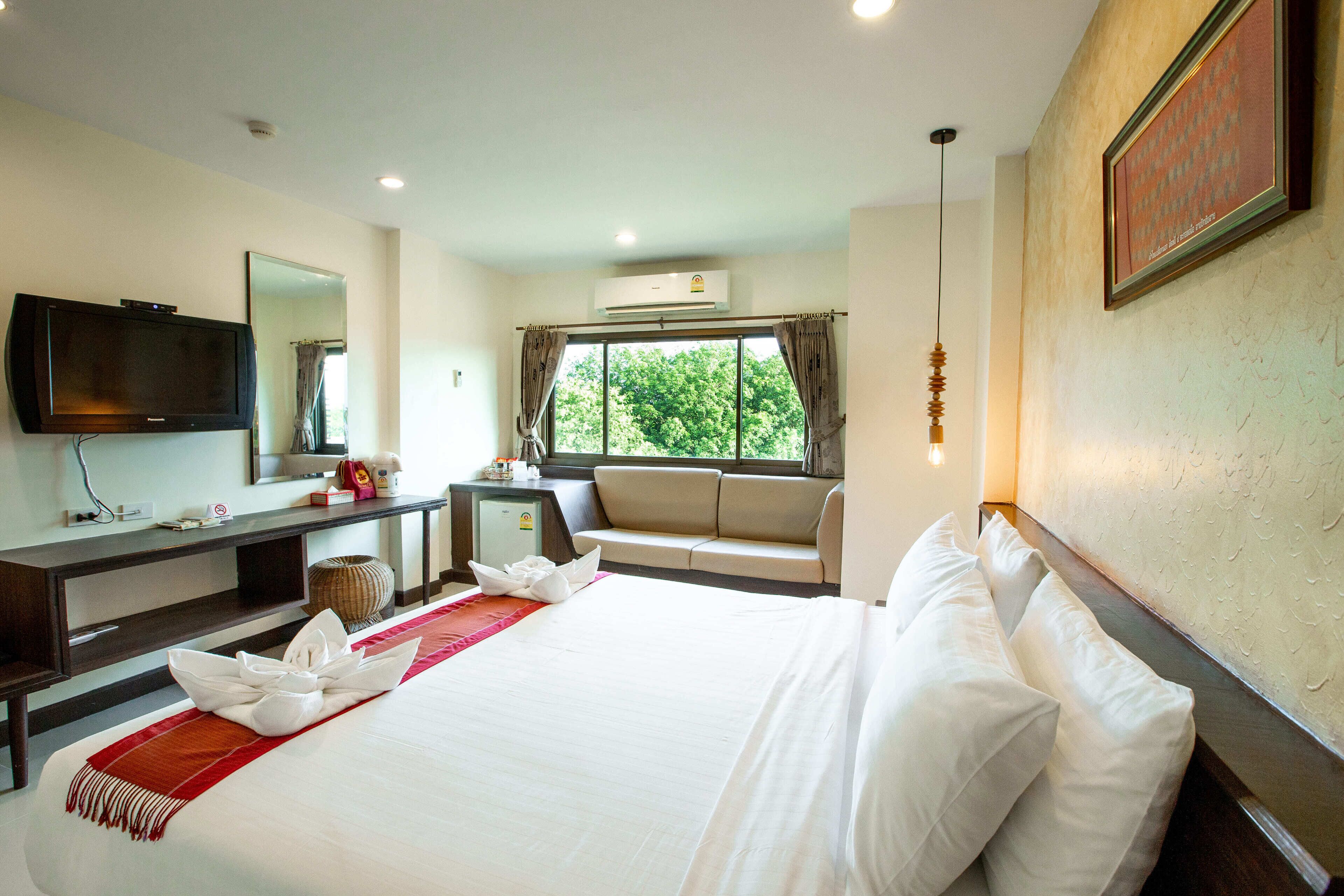 A hotel room with a large bed, a TV, a desk, and a window with curtains.