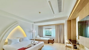 Habitación de hotel moderna con una cama grande, un escritorio, un televisor y una ventana con cortinas.