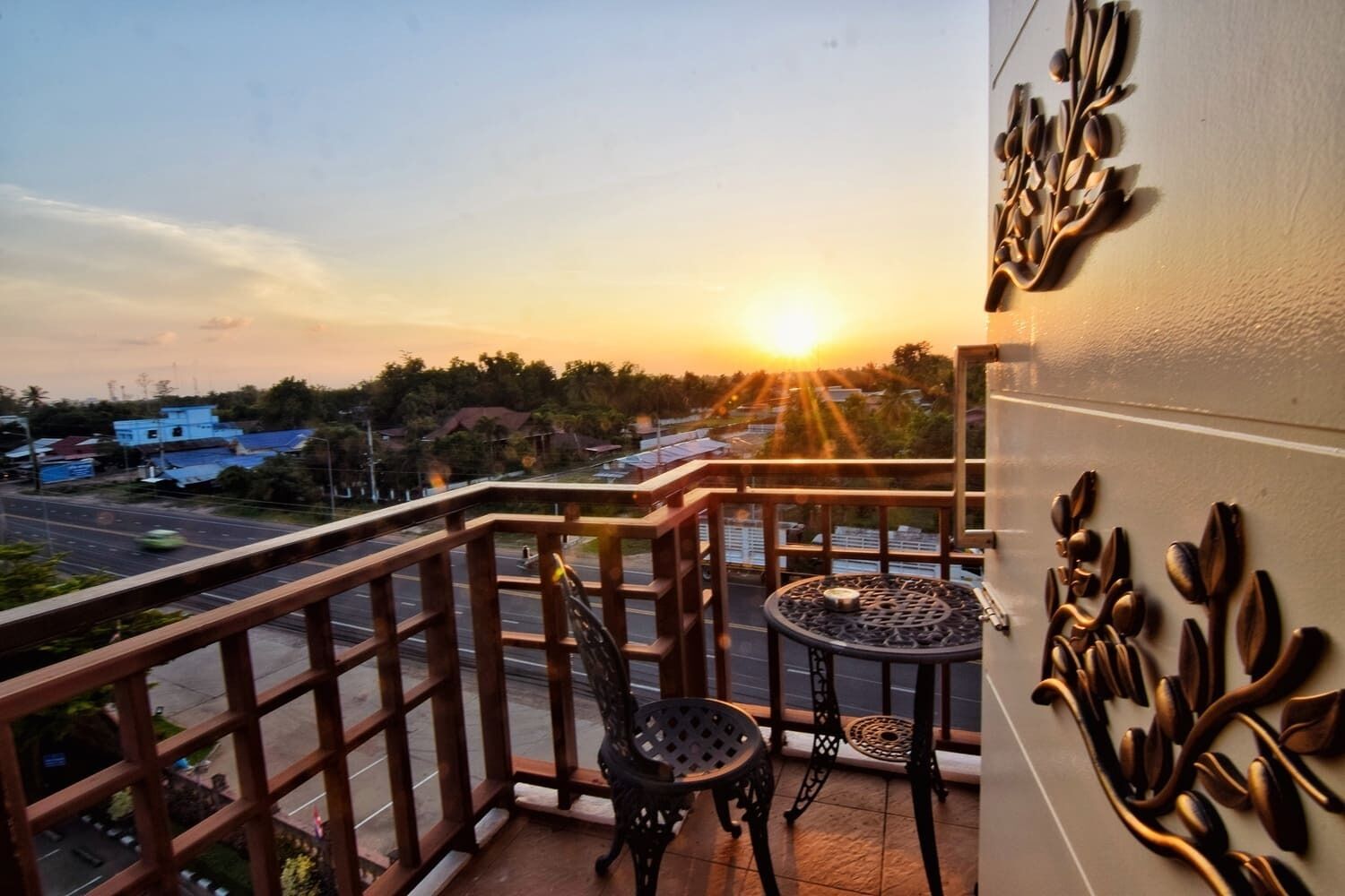 A balcony with a view of the sunset, a table, and chairs.