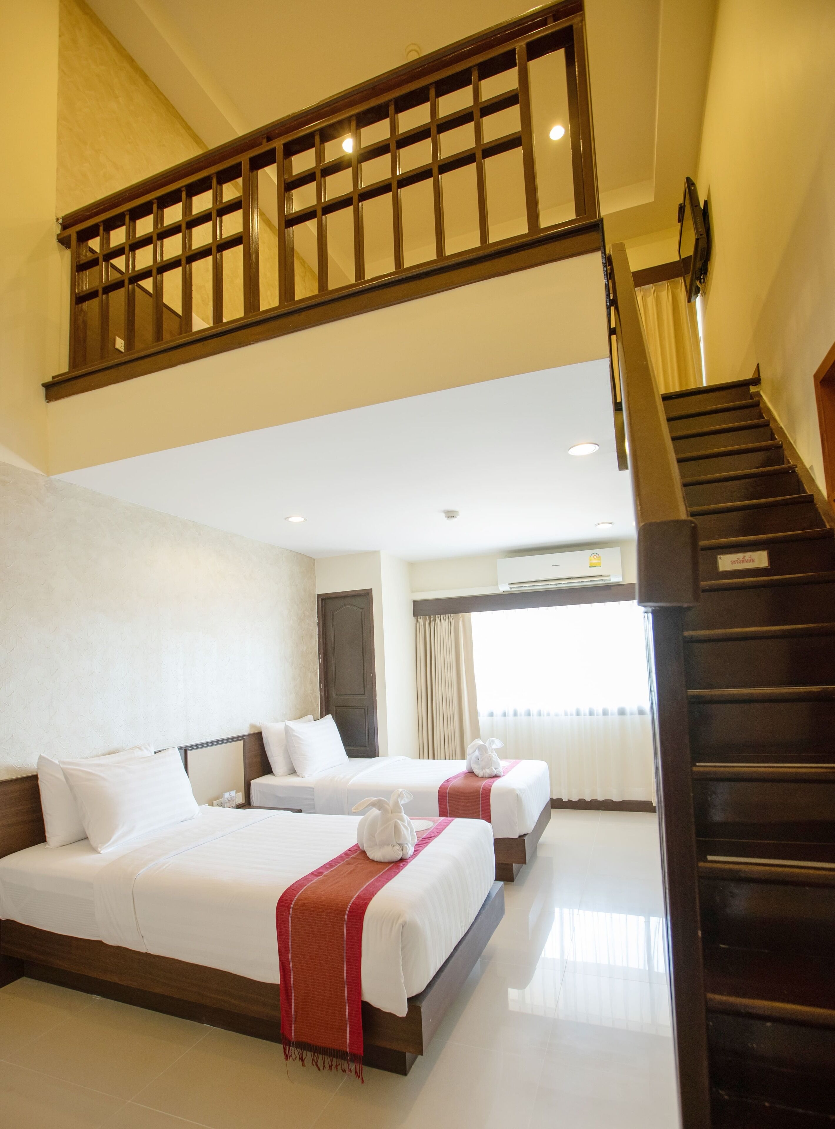 Habitación de hotel con dos camas, una escalera de madera y vistas al exterior.
