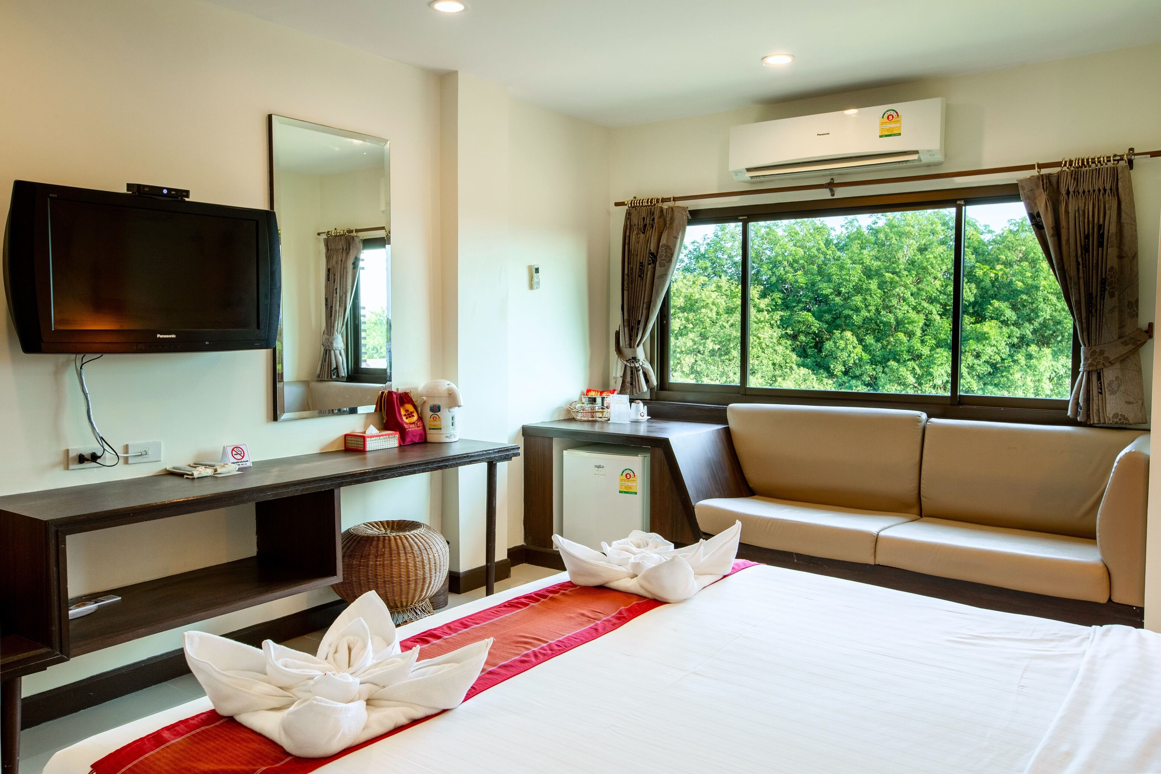 A hotel room with a bed, a TV, a desk, a sofa, and a window with a view of trees.