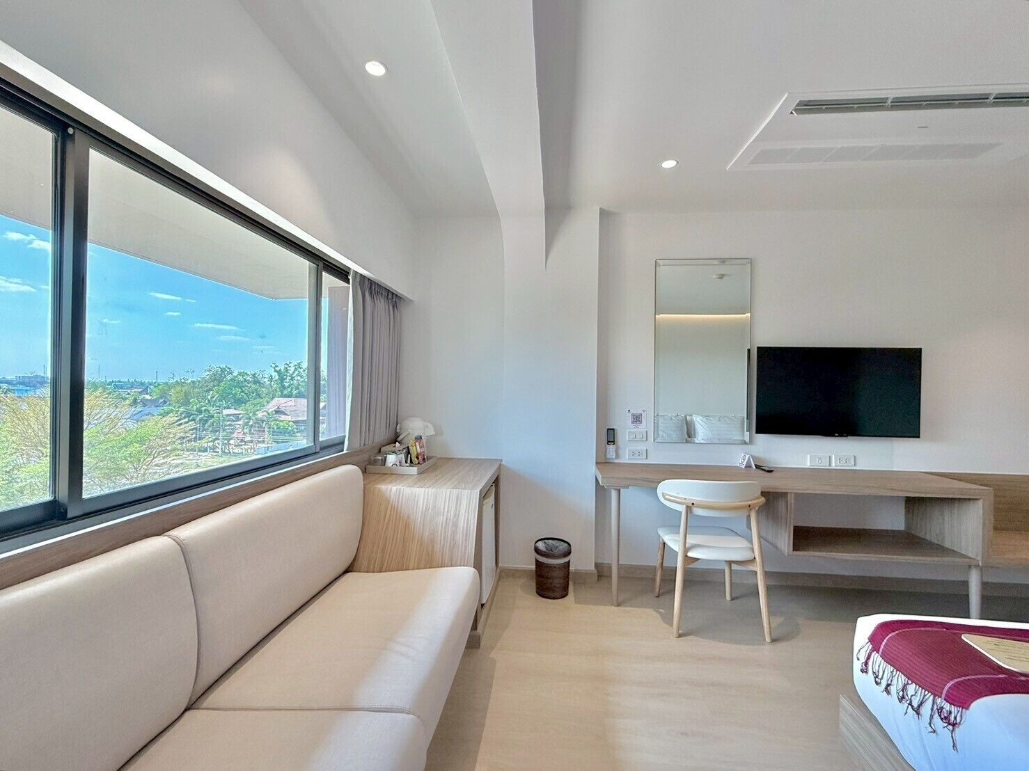 Een moderne hotelkamer met een bank, een bureau, een stoel, een televisie en een groot raam met uitzicht.